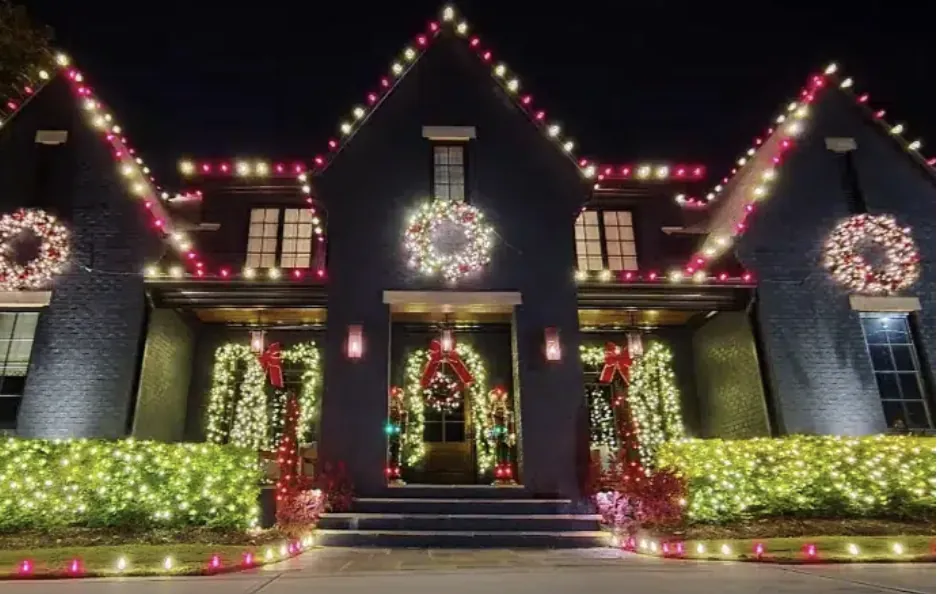 Brick house lit in red and white with wreaths spaced across the front.