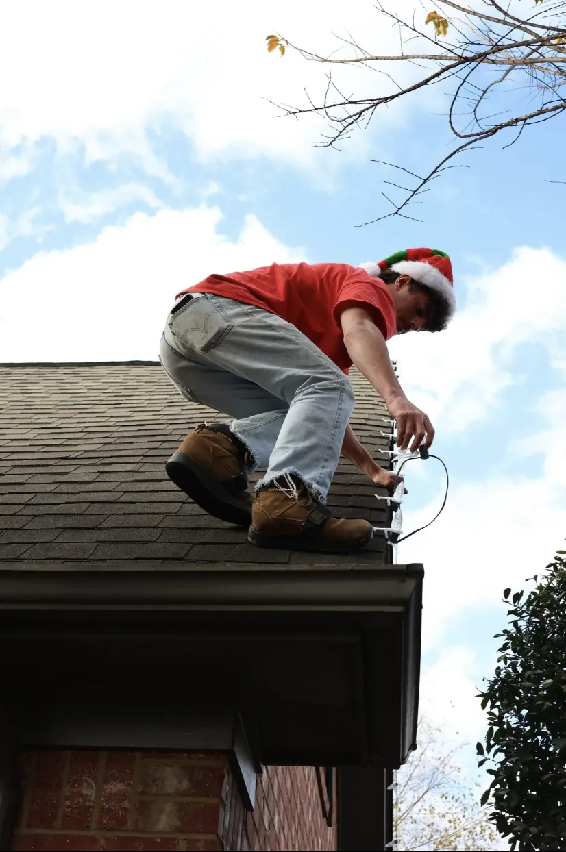 Installer at the gutter line of a brick house, working a light strand into place.