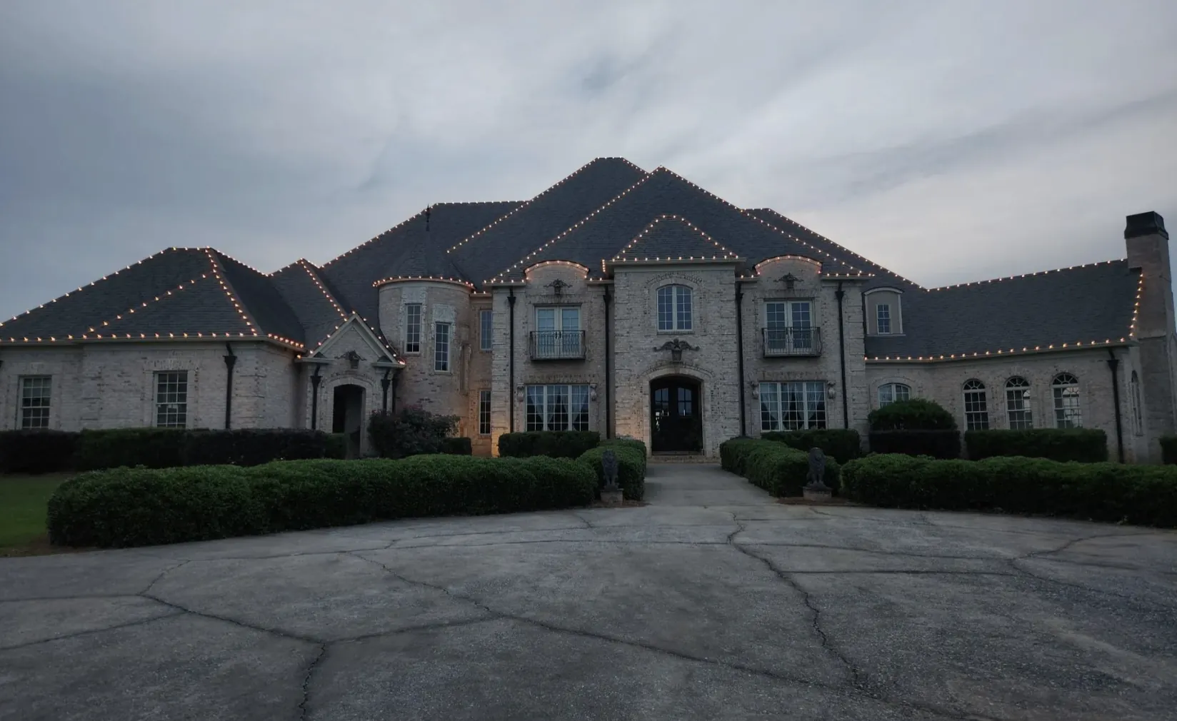 Large stone estate at dusk with lights tracing each roof peak above a circular driveway.