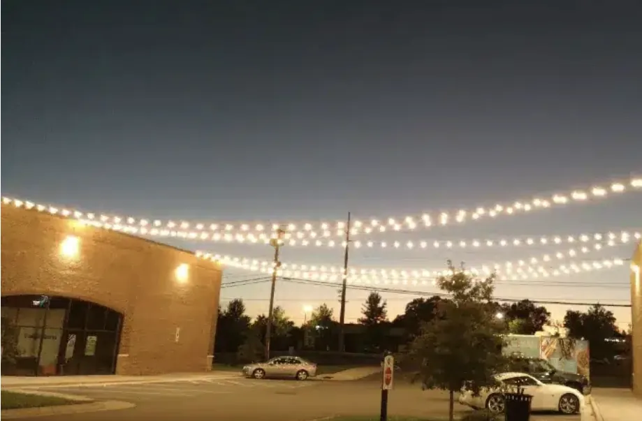 Row of brick storefronts with strands of white lights strung across the street.