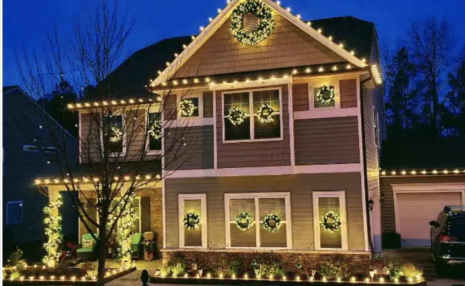 Two-story house at dusk with an even eave line of lights and wreaths in the front windows.